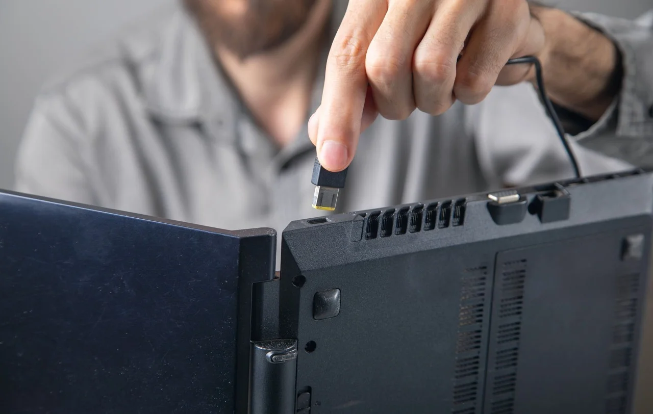 Person checking a laptop charging connection by inserting a charger into the laptop charging port to troubleshoot why the laptop is not charging.