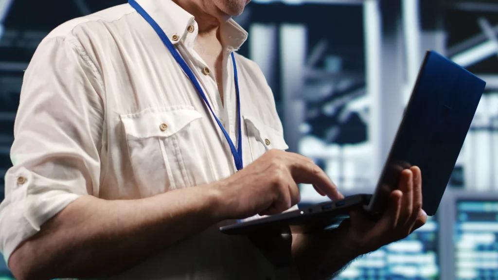 IT professional using a laptop to manage servers and monitor computer systems in a modern technology environment.