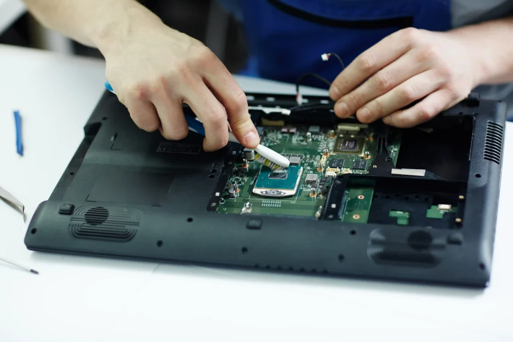Technician cleaning and inspecting the internal circuit board of a disassembled laptop during computer repair and maintenance. Select 83 more words to run Humanizer.