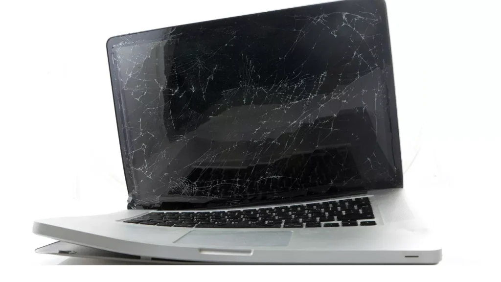 A laptop with a severely cracked and damaged screen, its casing bent and keyboard exposed. The image conveys a sense of disrepair and fragility.
