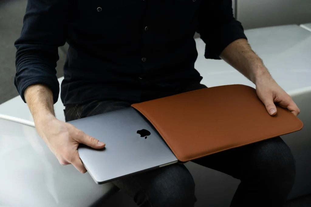 A person carefully placing a protective laptop sleeve over a closed laptop to help prevent damage during handling and storage.