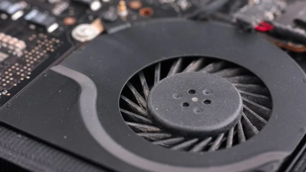 dusty-laptop-cooling-fan-close-up Close-up of a dusty computer cooling fan on a motherboard. The fan's blades are covered in dust, highlighting lack of maintenance and tech wear.