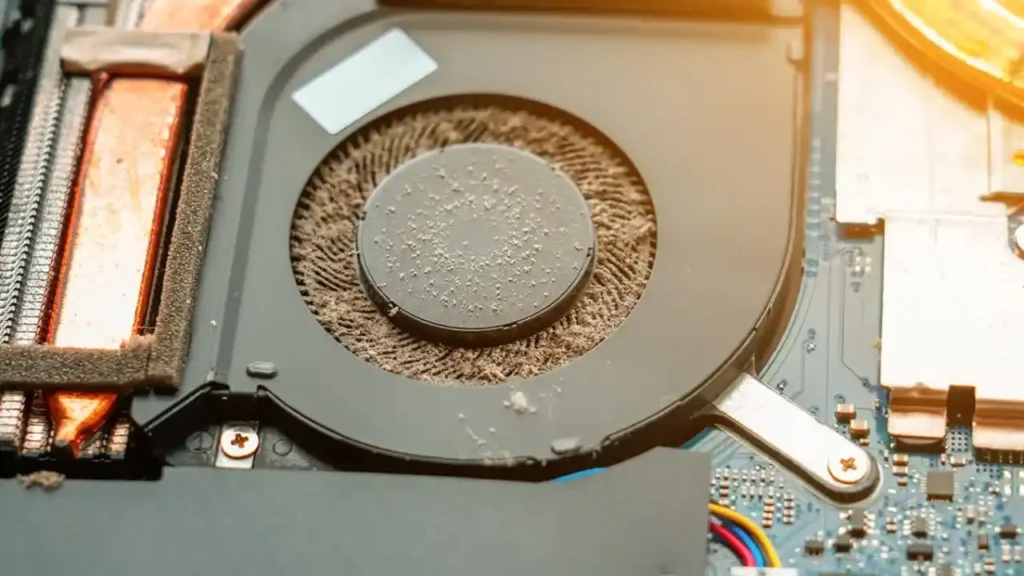 dusty-laptop-cooling-fan-hardware-maintenance Close-up of a dusty computer fan inside a laptop, surrounded by copper and aluminum components. The image conveys neglect and the need for cleaning.