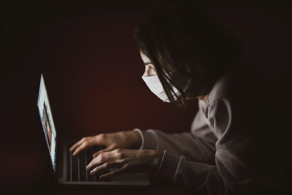 A person using a laptop in a dark room with a brightly illuminated screen, illustrating high screen brightness while working.