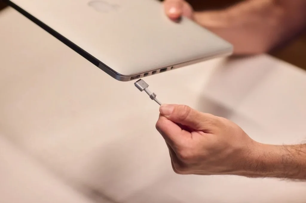 Hand connecting a charging cable to a laptop port, illustrating a possible charging connection issue.